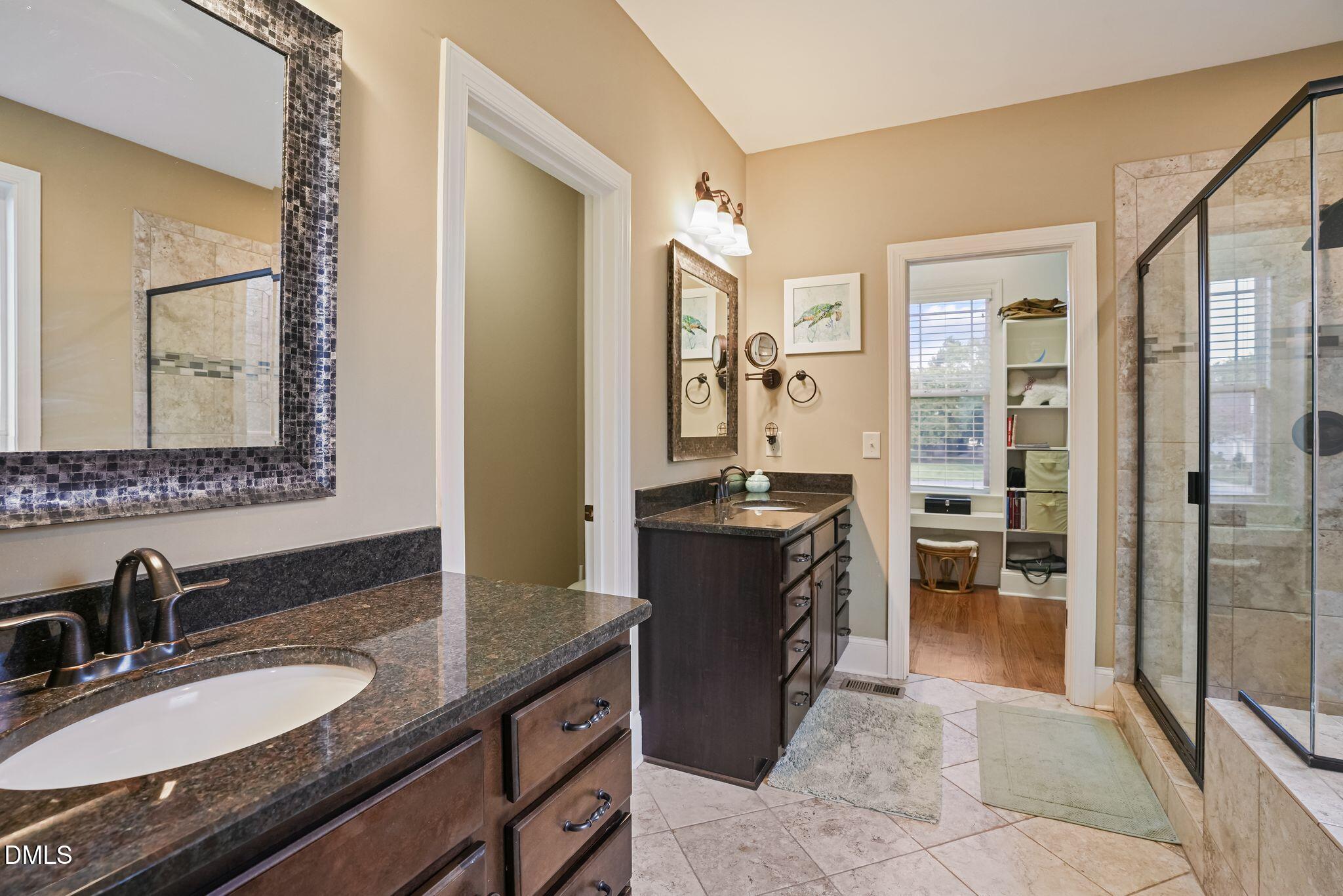 Bathroom with dual granite vanities, dark wood cabinetry, and a glass-enclosed tiled shower.