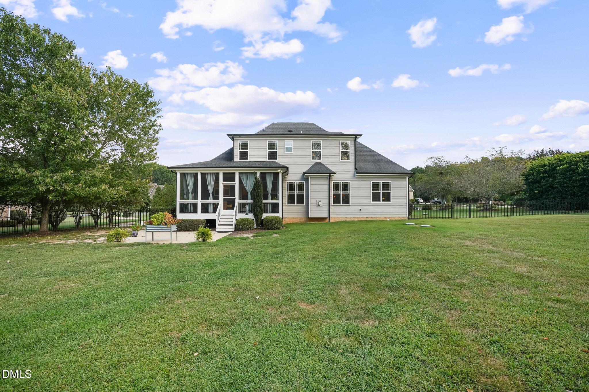 Two-story gray house with a screened porch overlooking a broad lawn and black fencing.