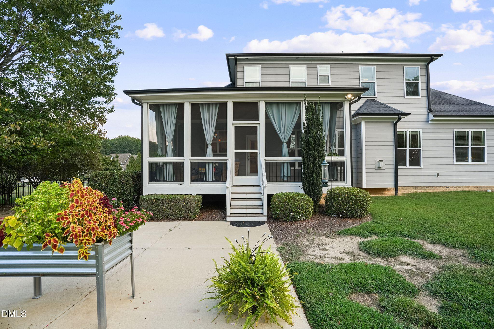 Two-story gray home with a screened porch, white steps, and a flower-filled planter beside the patio.