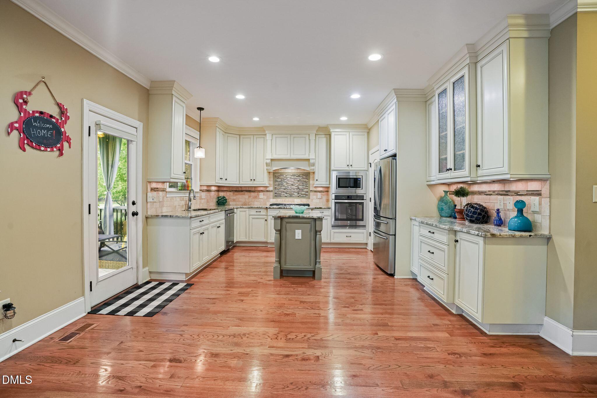Kitchen with cream cabinetry, a central island, stainless appliances, and warm hardwood floors.