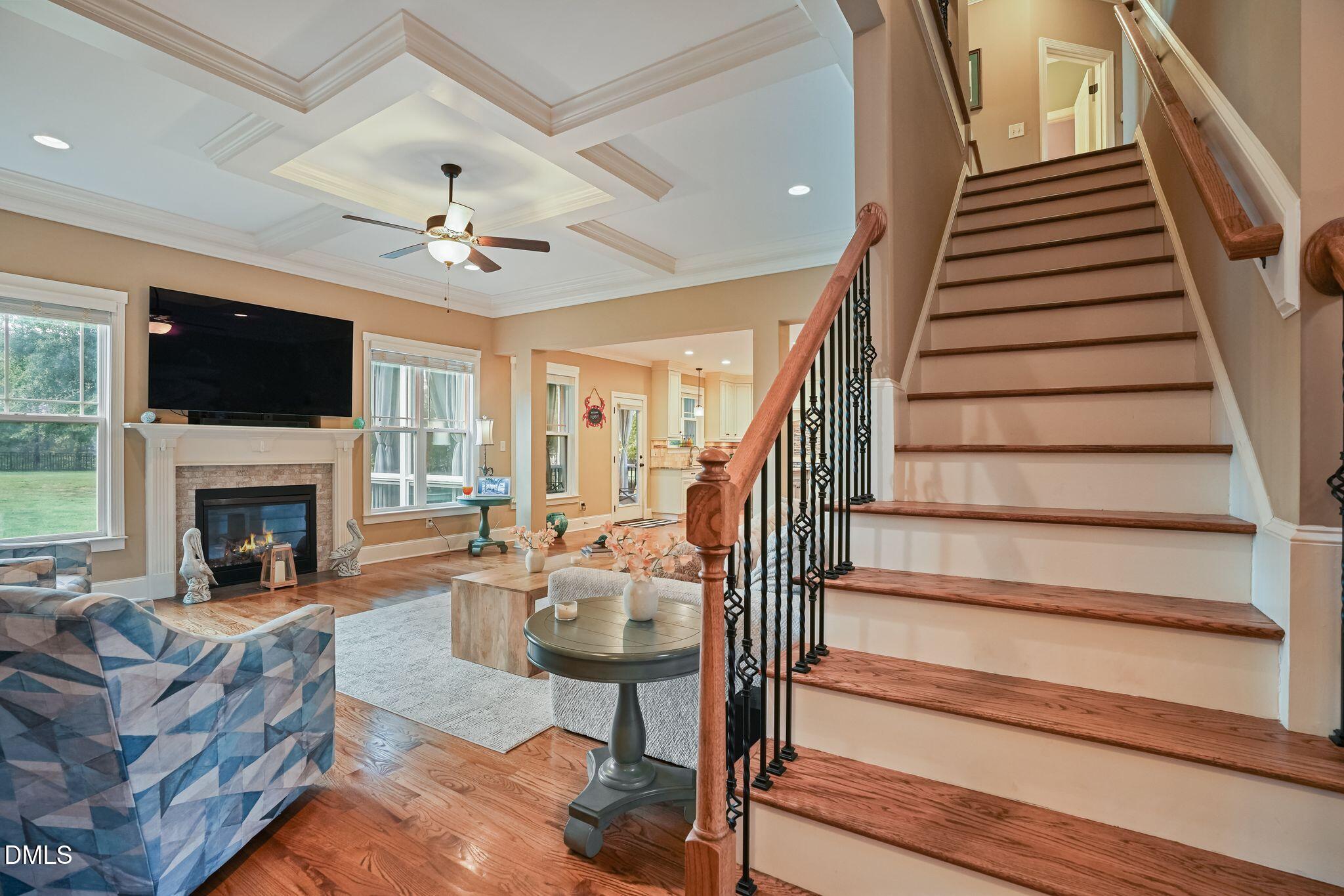 Living room with a fireplace and coffered ceiling beside a prominent wood staircase.