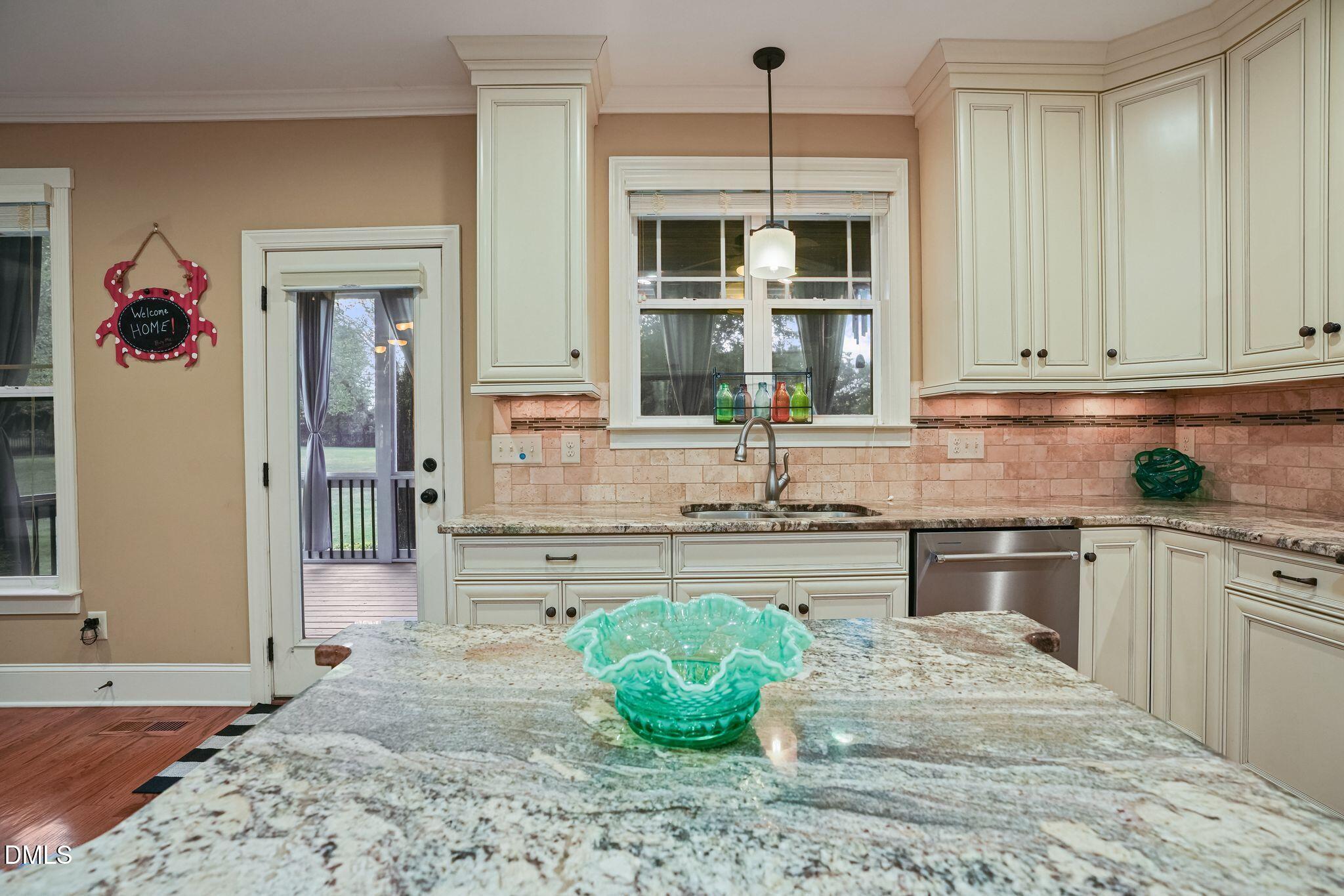 Kitchen with cream cabinetry, pink tile backsplash, and a granite island with a turquoise glass bowl.
