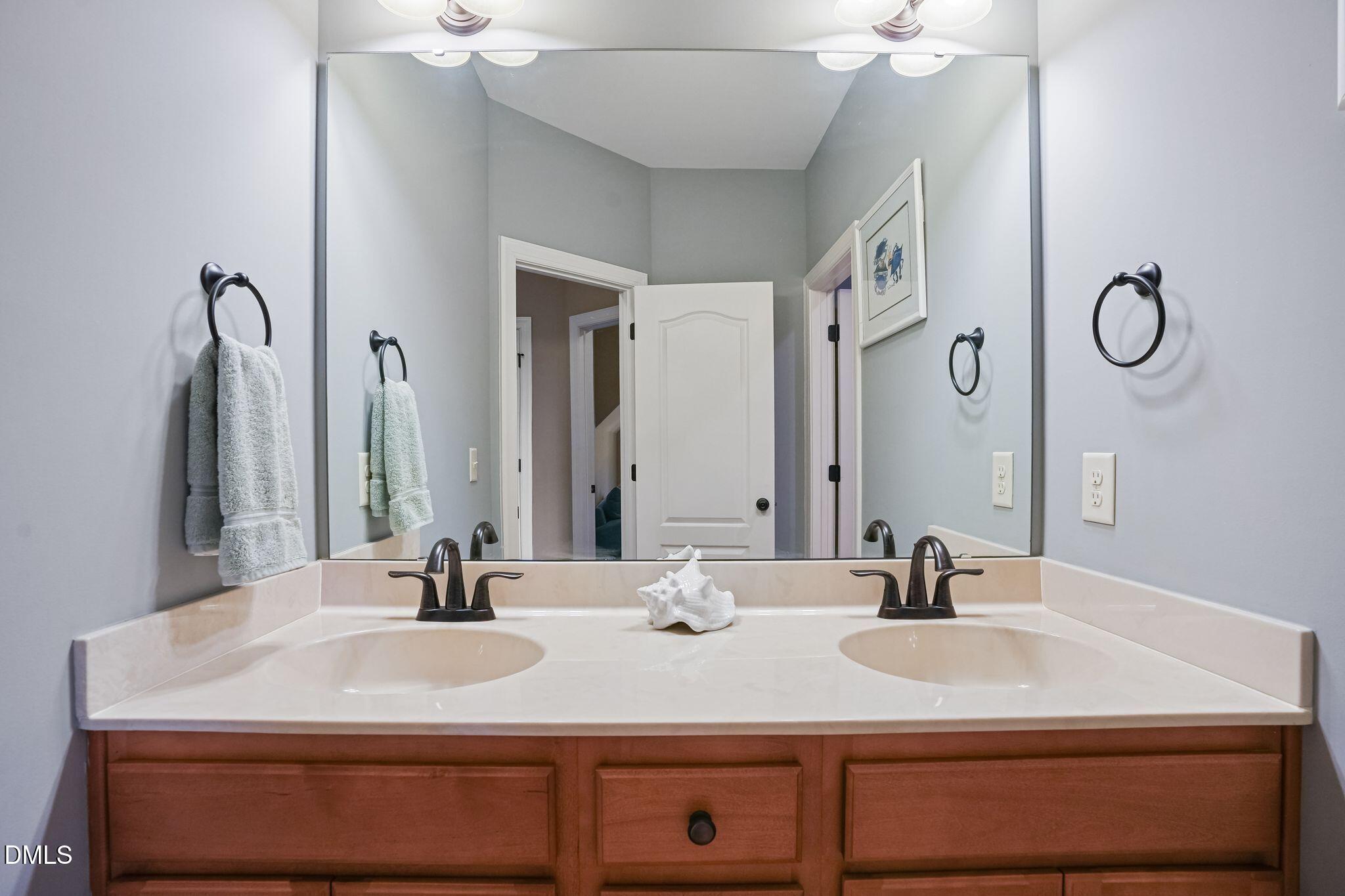 Bathroom vanity with double sinks, dark faucets, a large mirror, and warm wood cabinets.