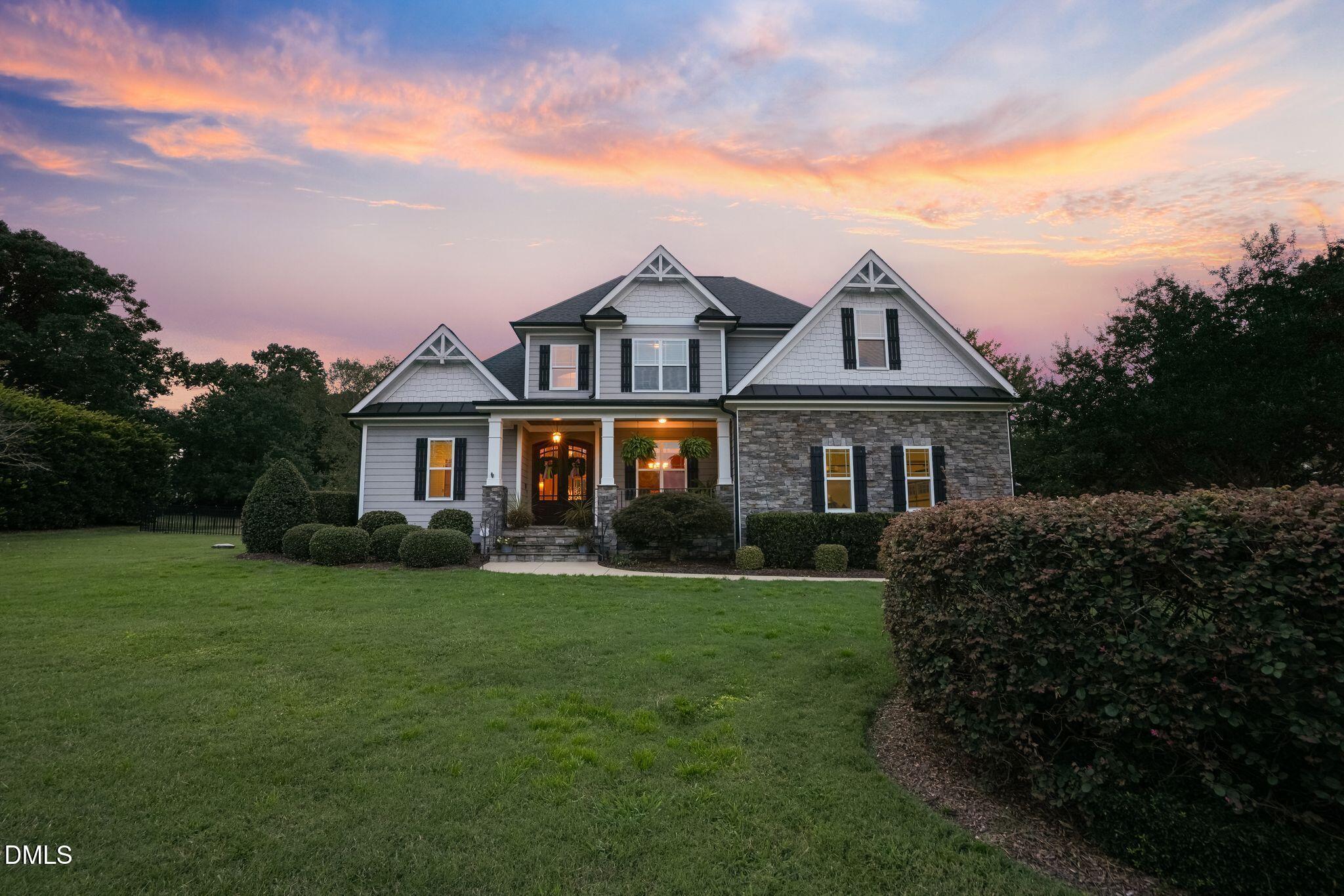 Two-story gray-and-stone house with a covered entry and landscaped lawn at dusk.