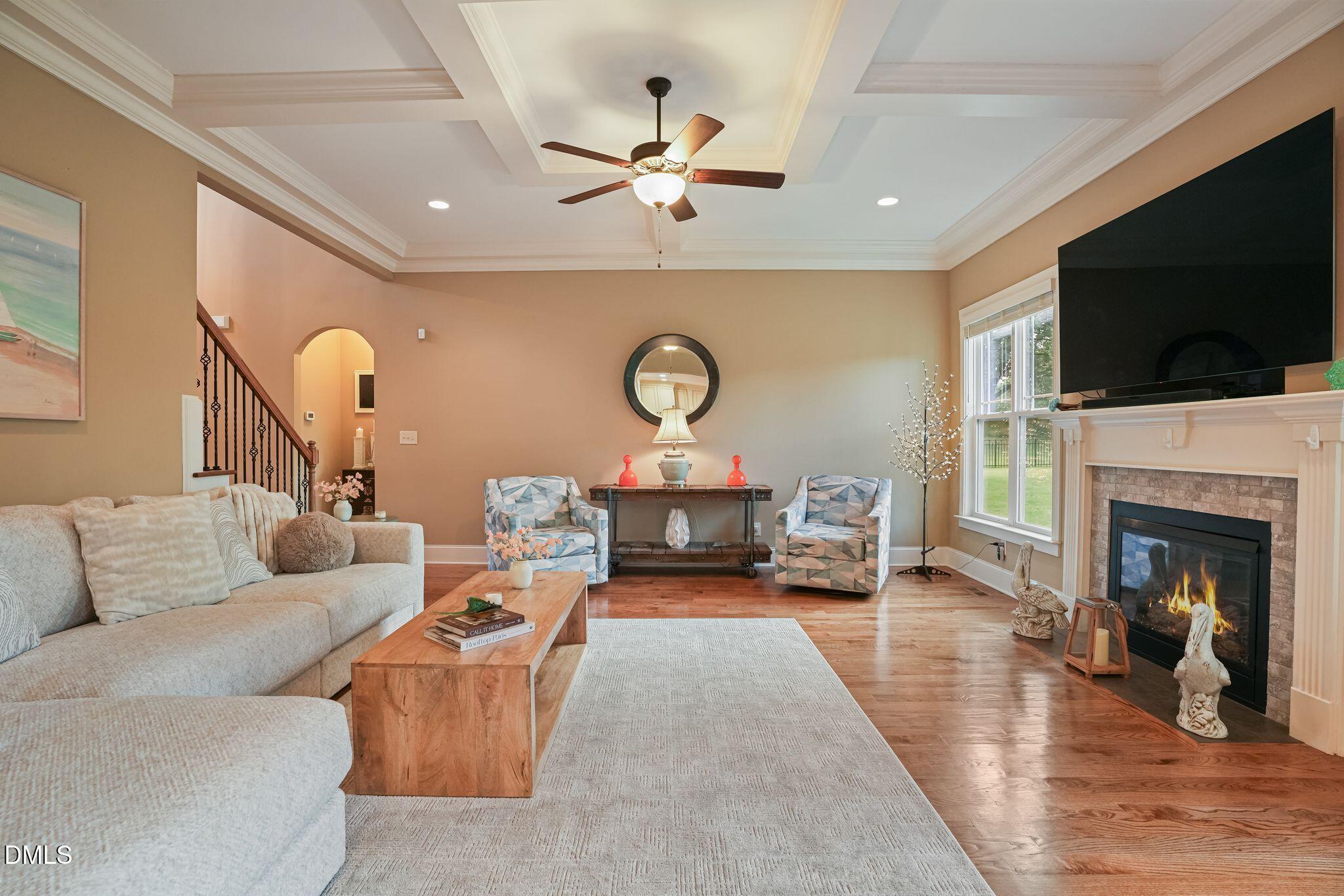 Living room with a beige sectional, patterned armchairs, and a lit fireplace beneath a wall-mounted television.
