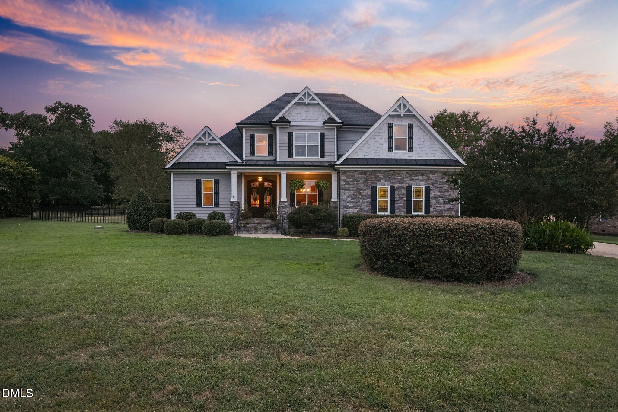 Two-story gray home with stone facade and landscaped lawn beneath a colorful dusk sky.