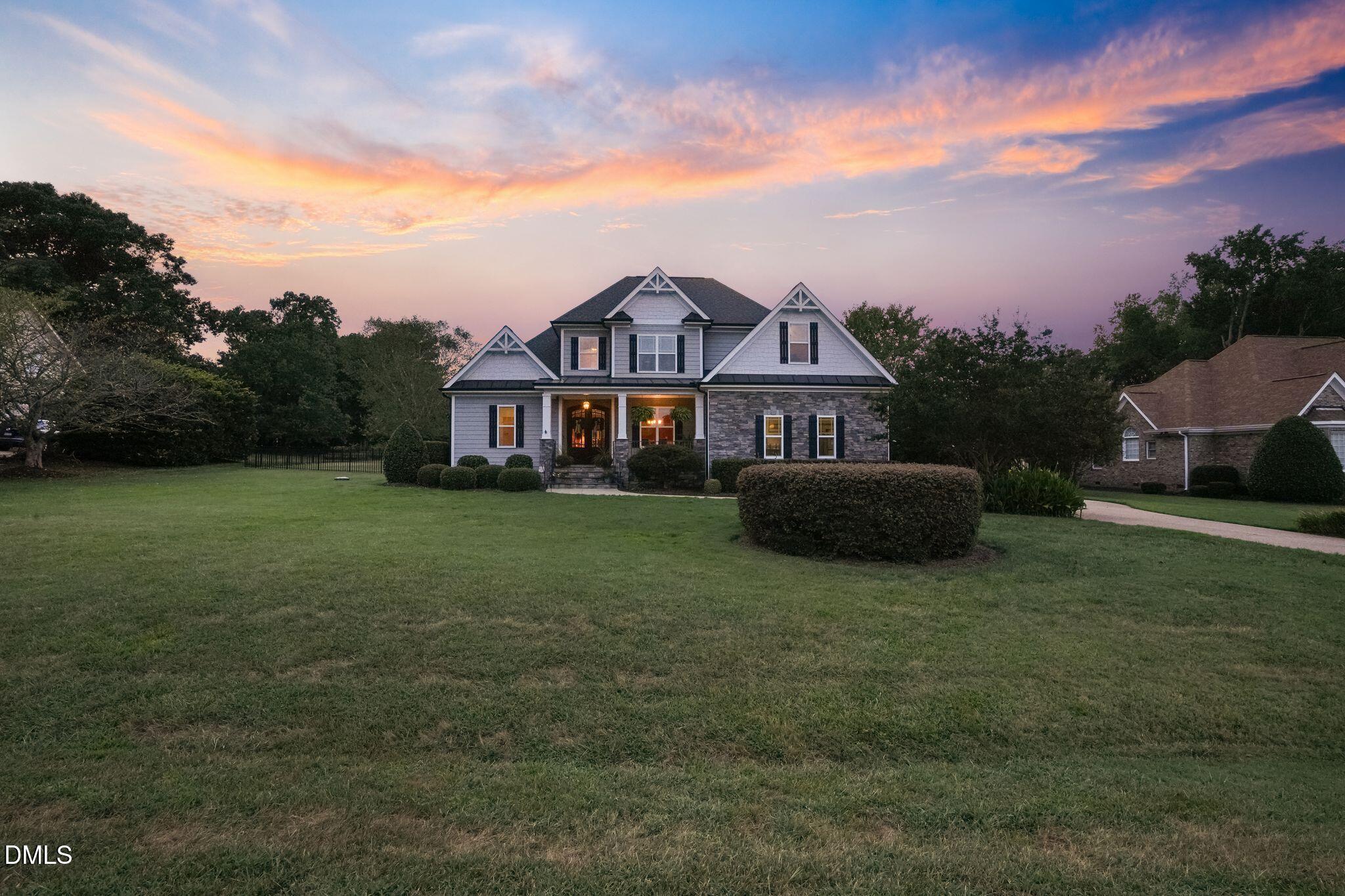 Two-story gray house with stone accents and a broad lawn beneath a colorful dusk sky.
