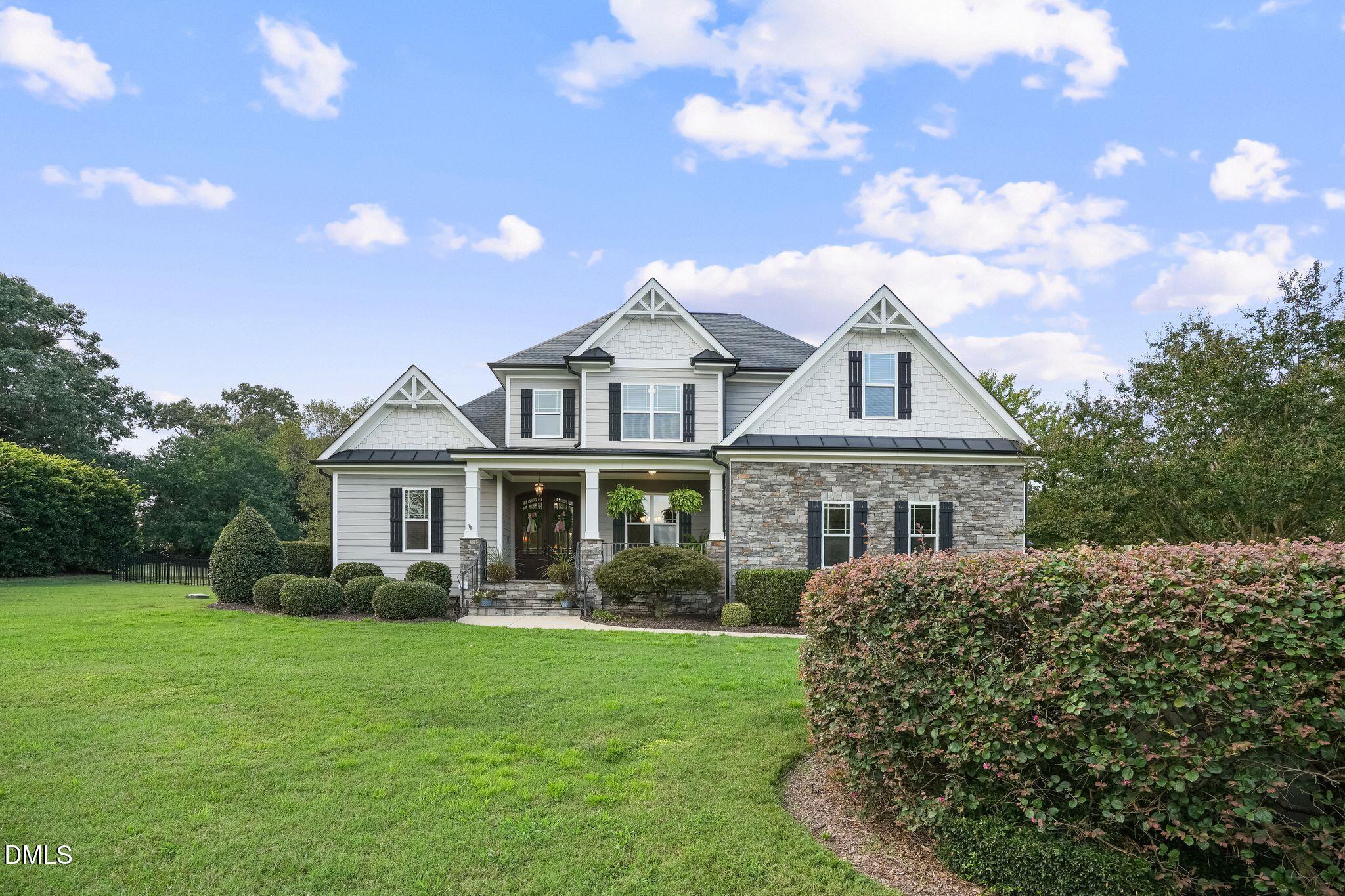 Gray two-story home with stone facade, covered porch, and broad green lawn.