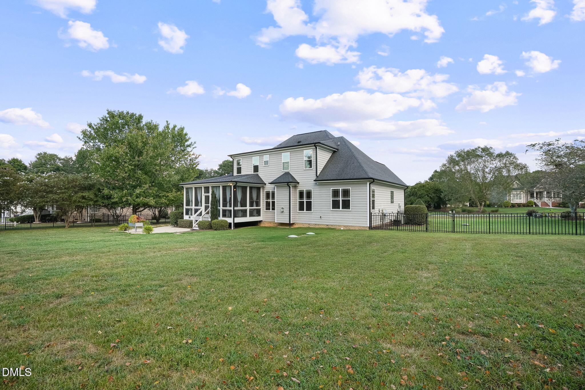 Rear of a two-story gray house with a screened porch and fenced grassy backyard.