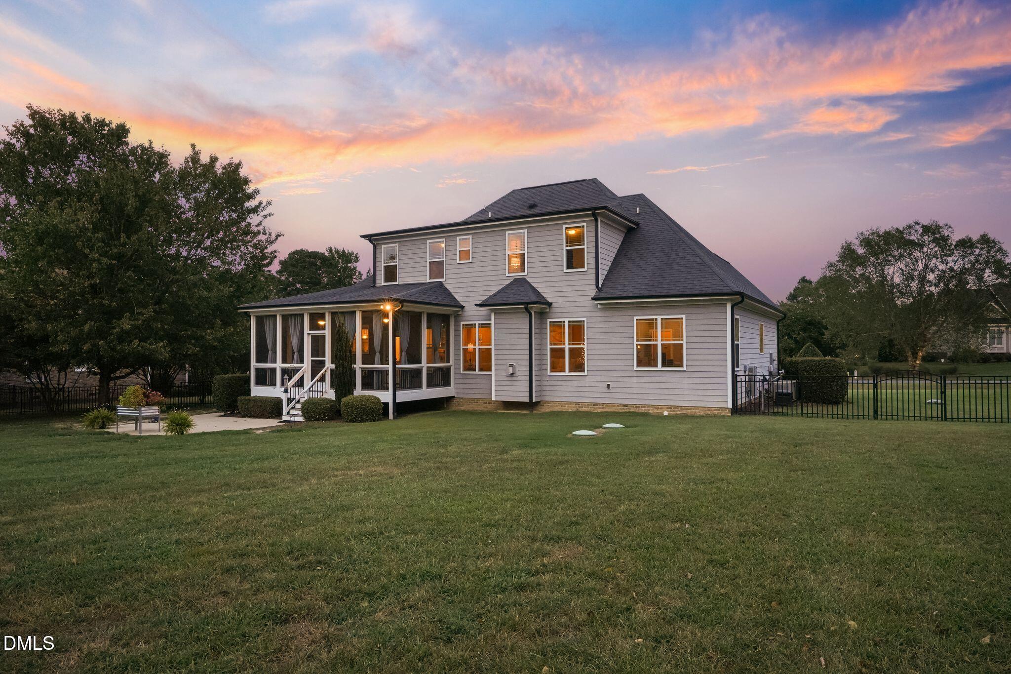 Two-story gray house with a screened porch and fenced lawn at dusk.