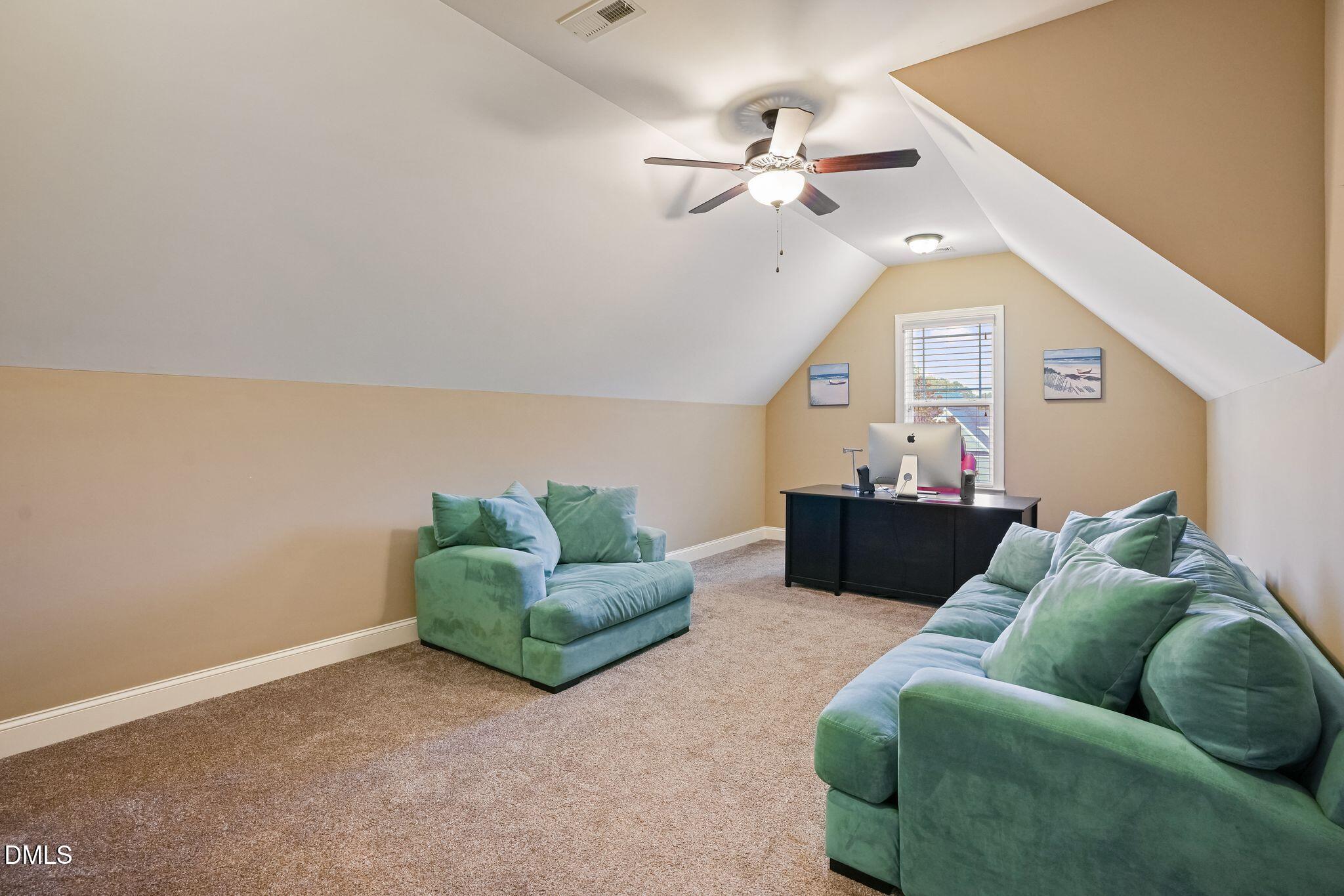 Furnished bonus room with green sofas, a desk beneath the window, and a sloped ceiling.