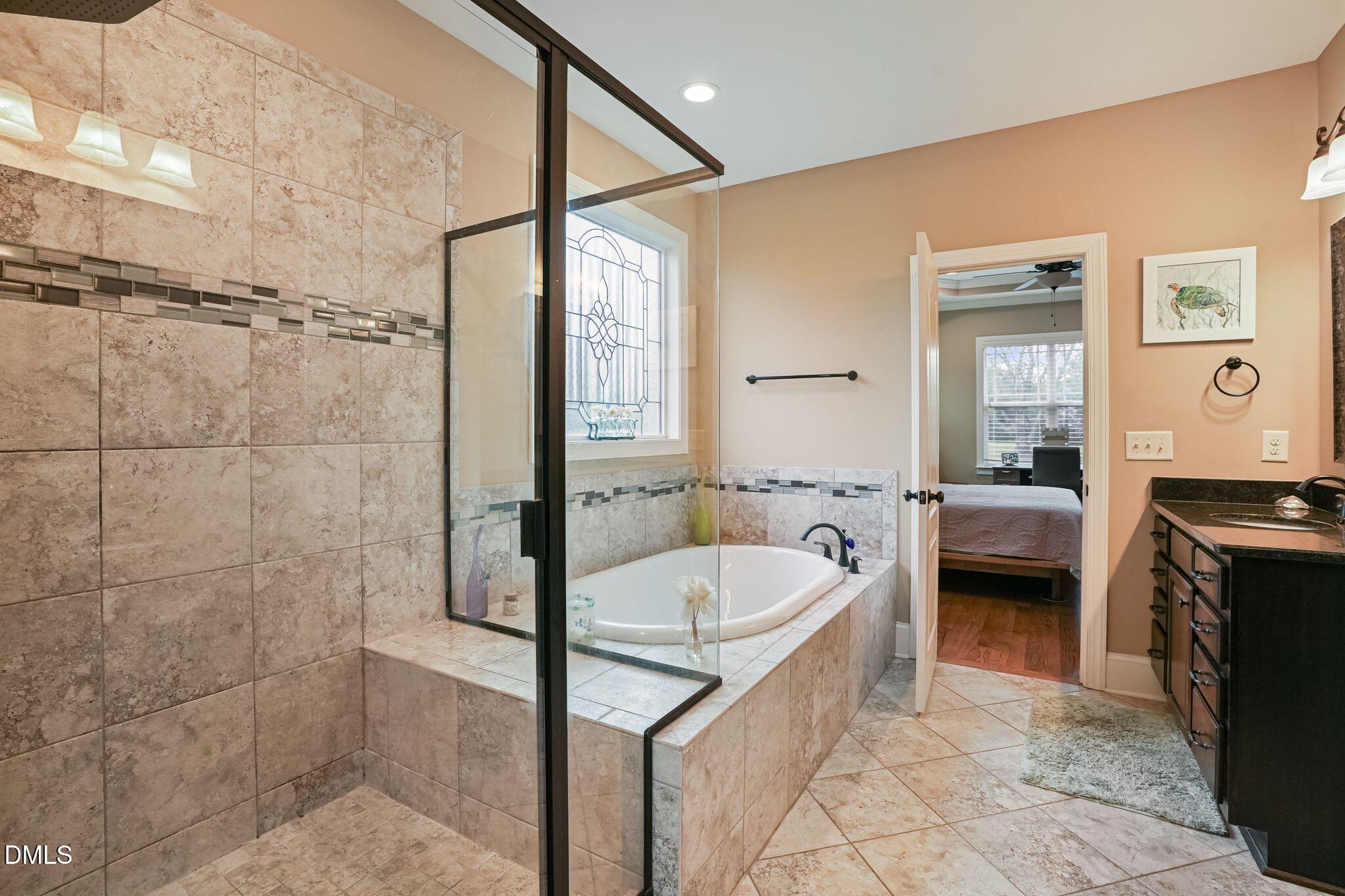 Bathroom with a tiled soaking tub, glass shower partition, and dark vanity