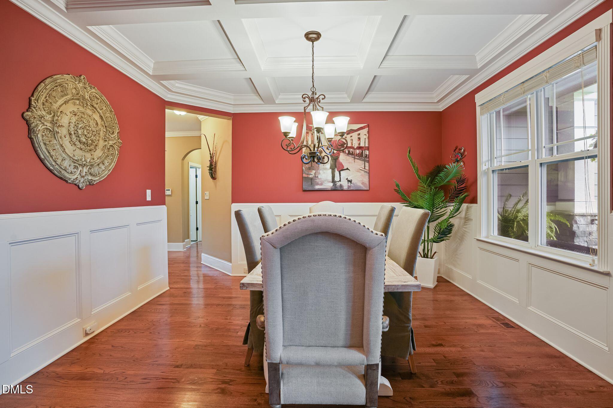 Dining room with a coffered ceiling, red walls, hardwood floors, and a long table by large windows.