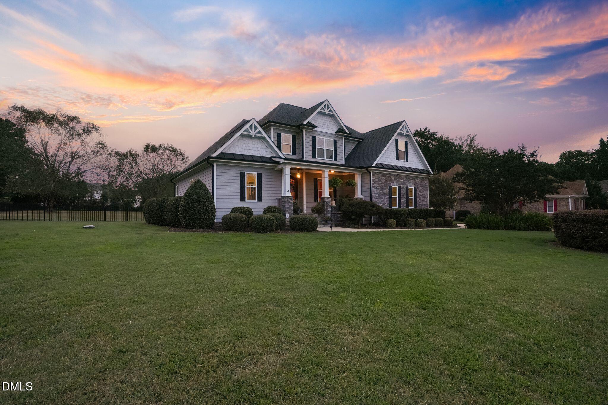 Two-story gray home with stone accents and a covered porch beneath a colorful dusk sky.