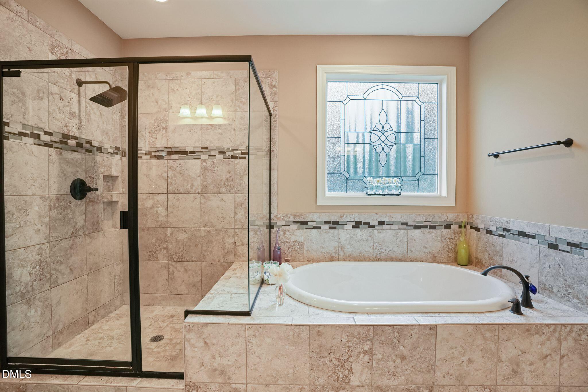 Bathroom with a tiled soaking tub, glass-enclosed shower, and decorative stained-glass window.