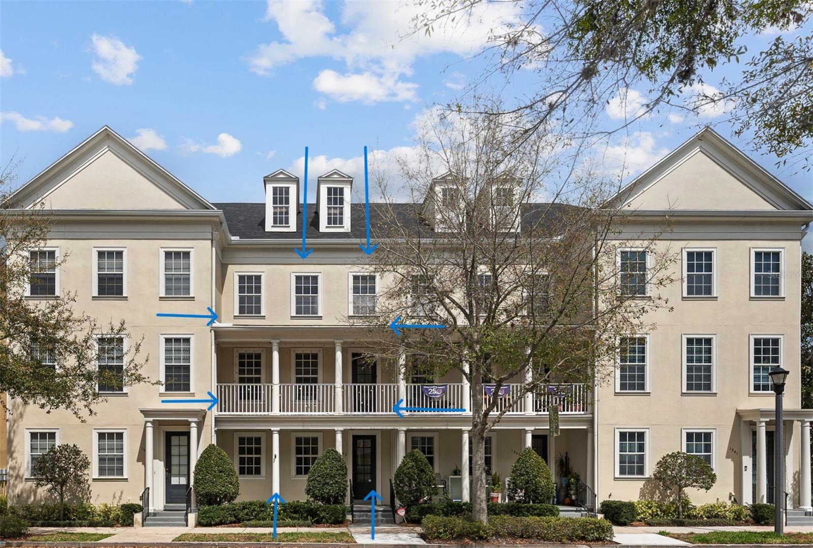 Cream-colored townhouses with covered porches and balconies, marked with blue arrows.