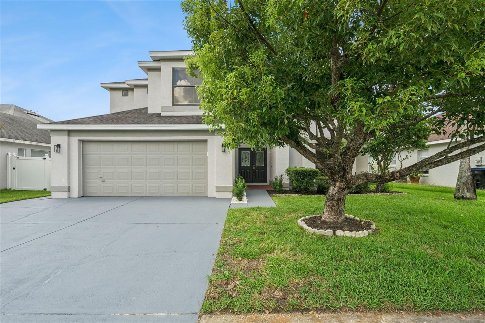 Two-story house with a double garage, broad driveway, and a large shade tree in the front lawn.