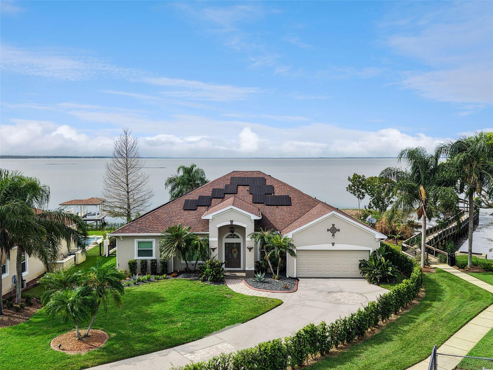 Lakeside home with rooftop solar panels, a landscaped lawn, and a dock.