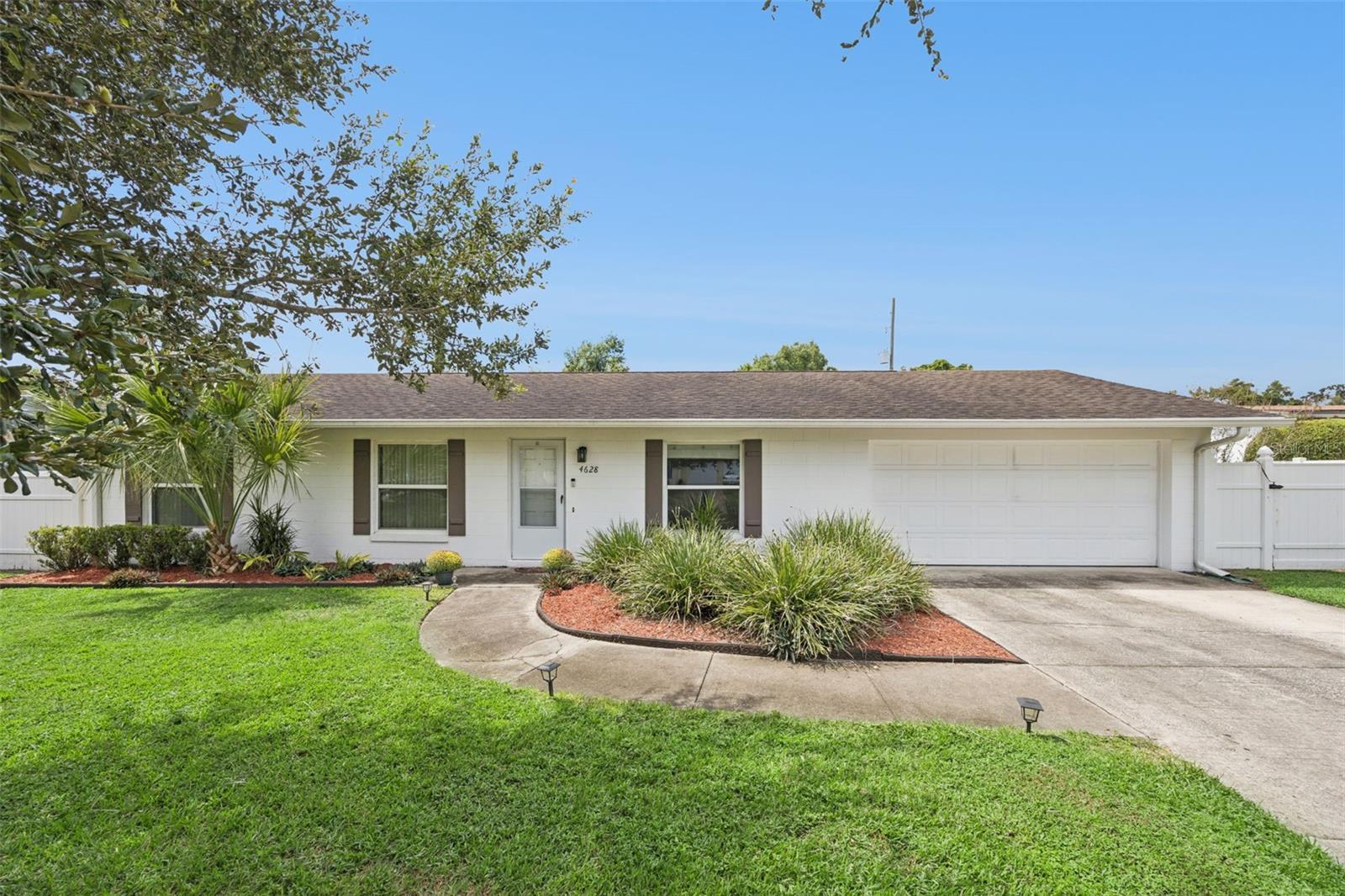 Single-story white house with an attached garage, landscaped beds, and a green front lawn.