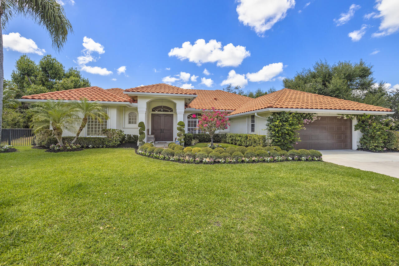 Single-story stucco home with terracotta roof, arched entry, attached garage, and landscaped lawn.