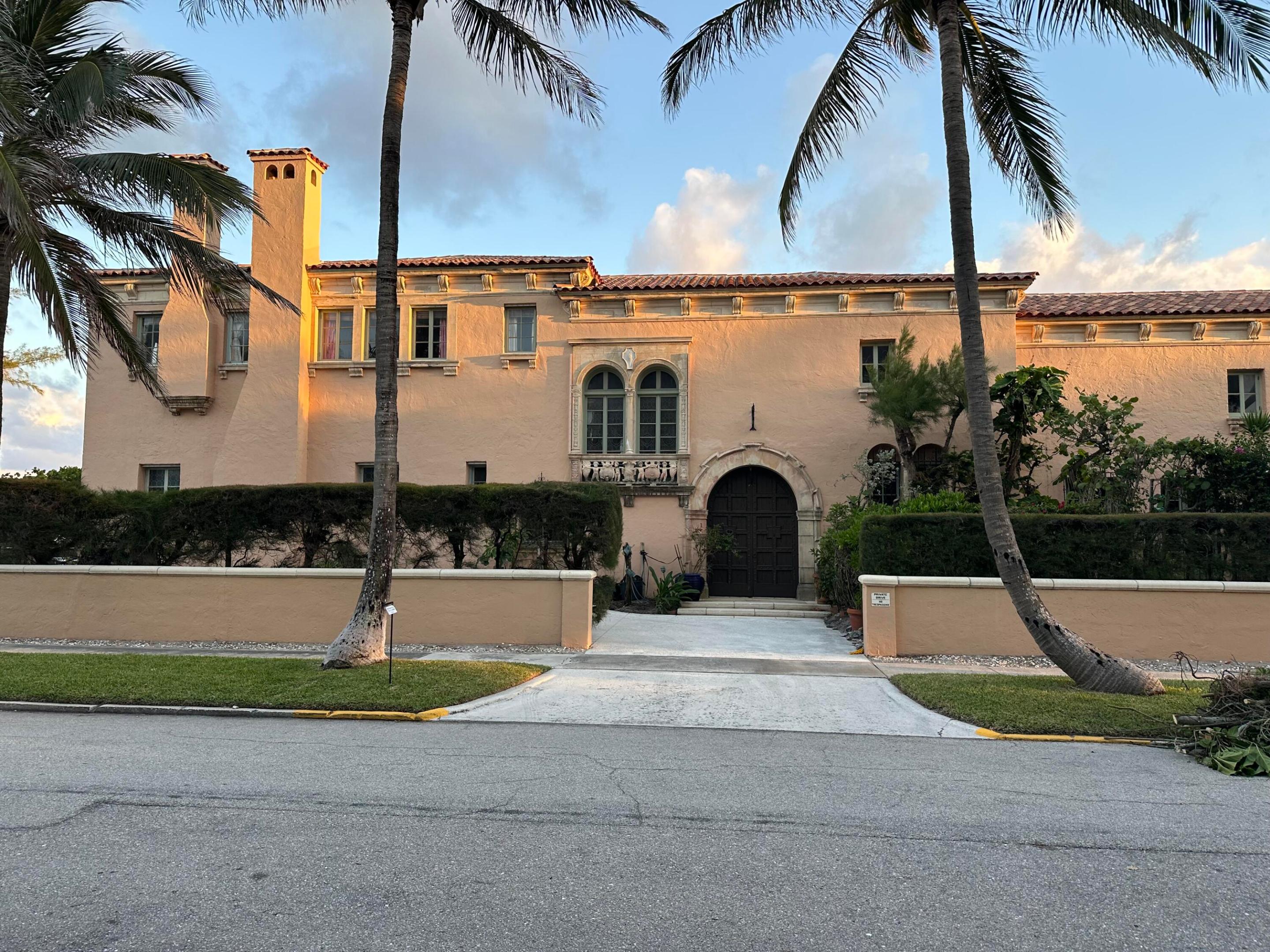 Mediterranean-style home with a tower, arched entrance, and palm trees in warm evening light.