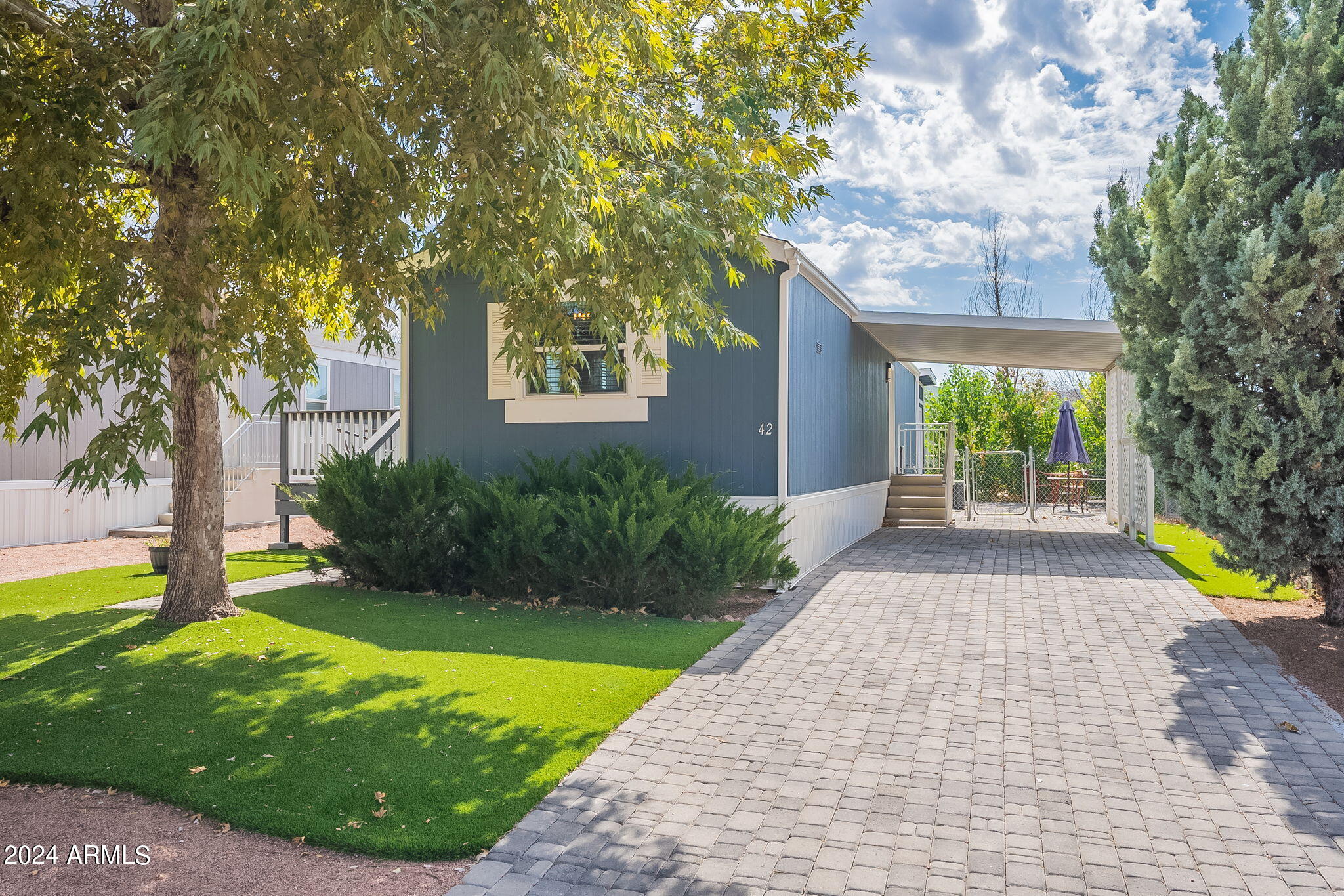 Blue-sided home marked 42 with a covered carport and paved driveway.