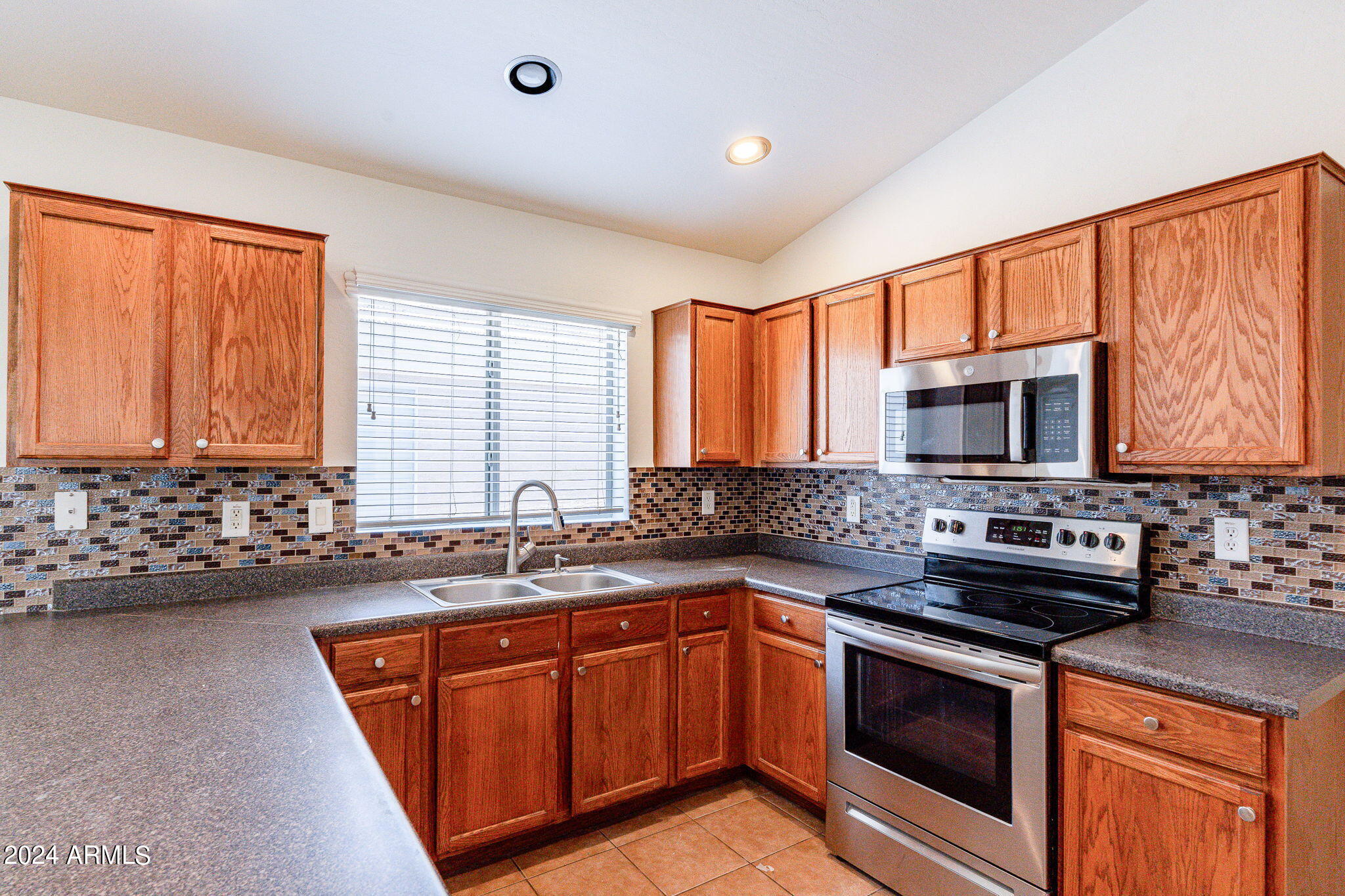 Kitchen with reddish wood cabinets, mosaic tile backsplash, double sink, and stainless steel appliances.