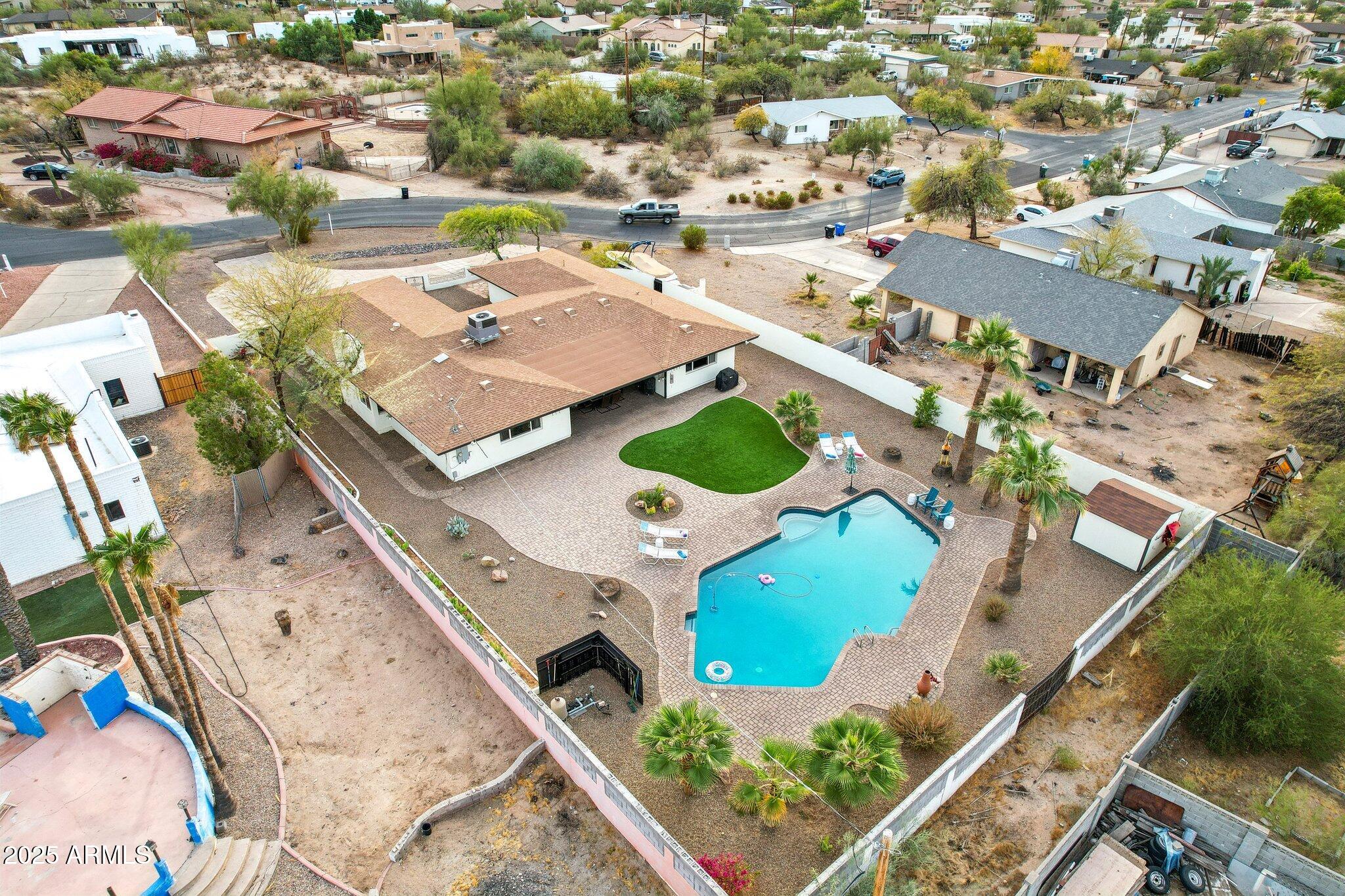 Aerial view of a single-story home with a backyard pool, paved patio, lawn, and palm trees.