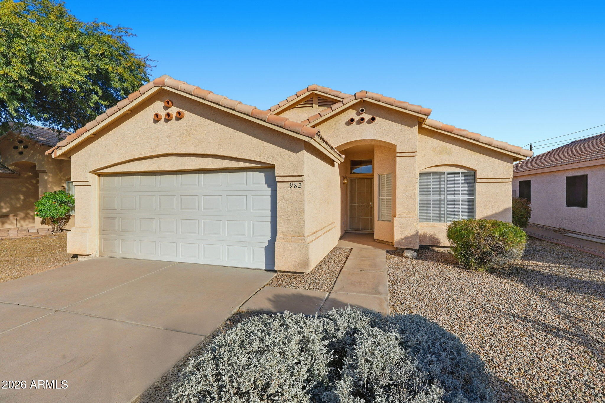 Tan stucco home with a tile roof, arched entry, double garage, and gravel landscaping.