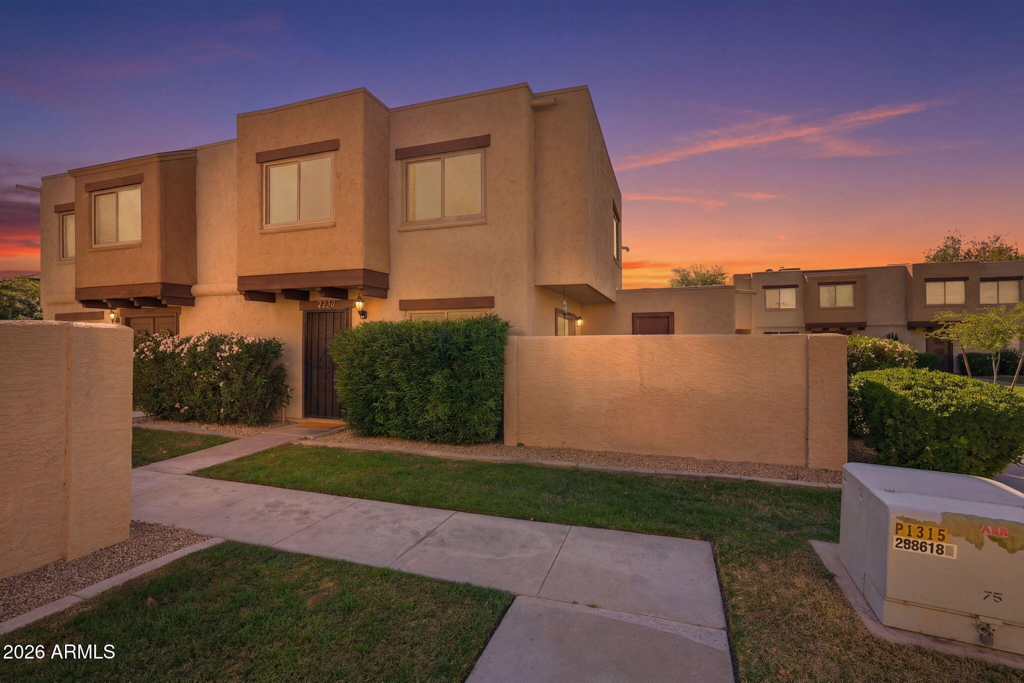 Tan two-story attached home with a stucco wall and front walkway at sunset.