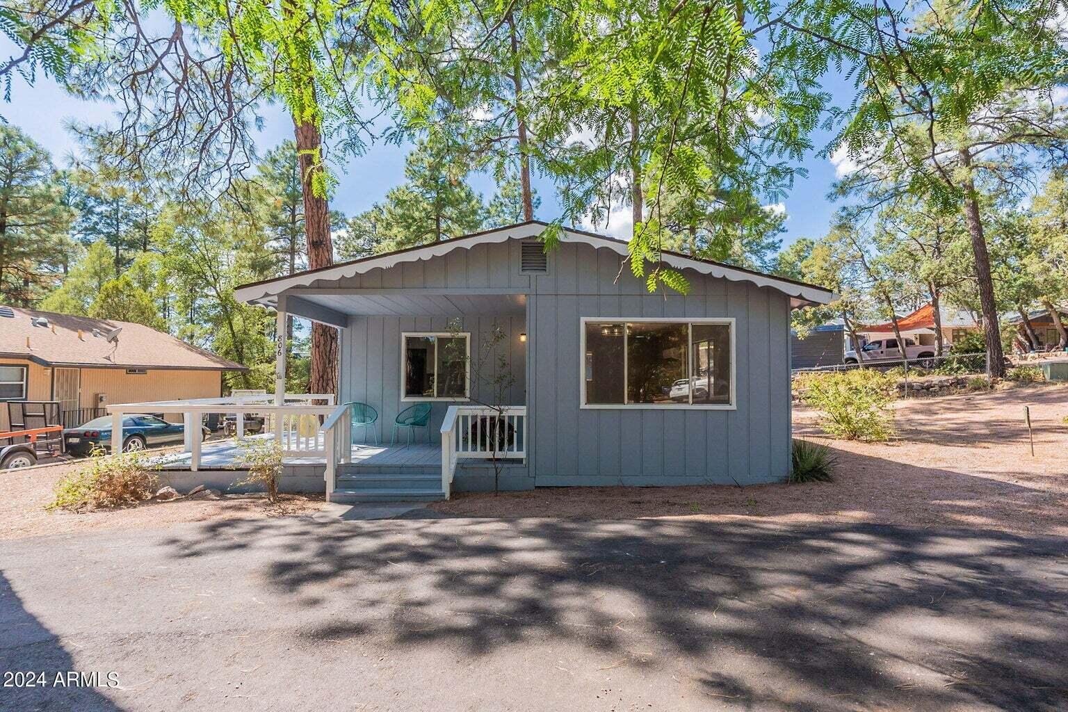 Gray home with a covered porch and white railings beneath mature trees.
