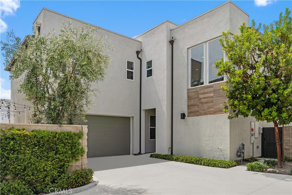 Modern two-story stucco house with a gray garage, wide driveway, and wood-look exterior accent.