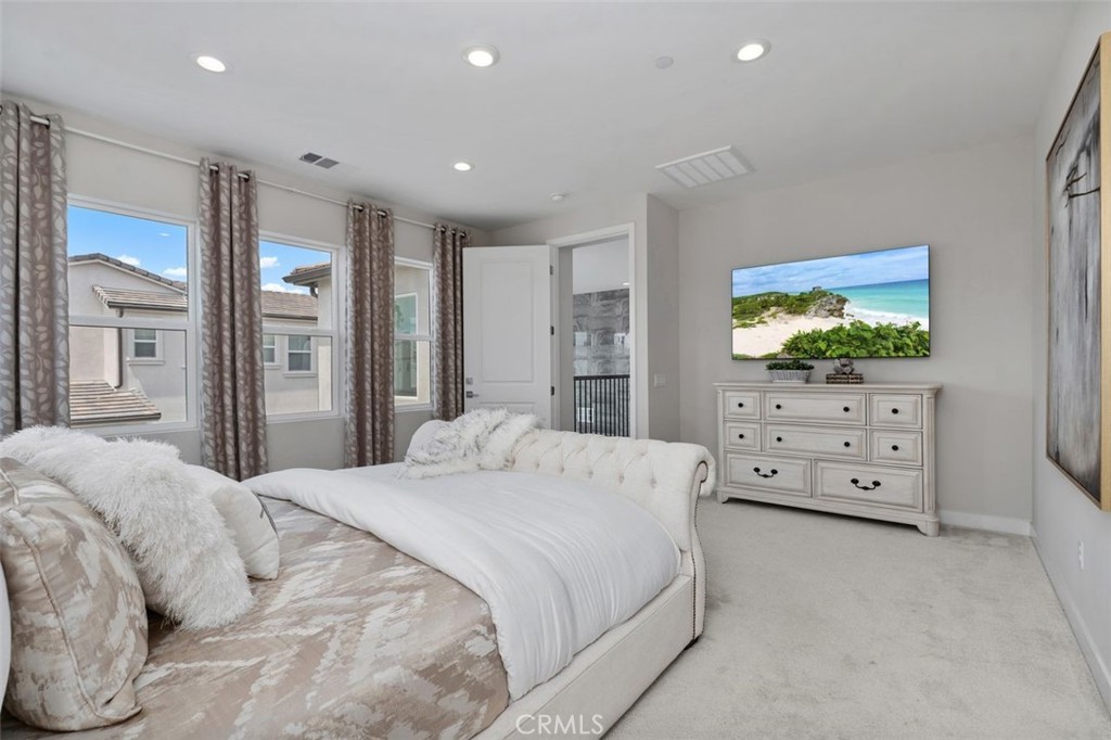 Bedroom with a large upholstered bed, patterned curtains, and a white dresser beneath a television.