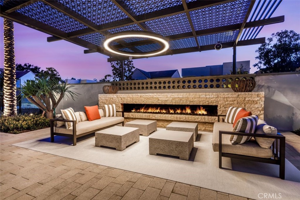 Outdoor patio lounge with cushioned seating, stone fireplace, and patterned pergola at dusk.