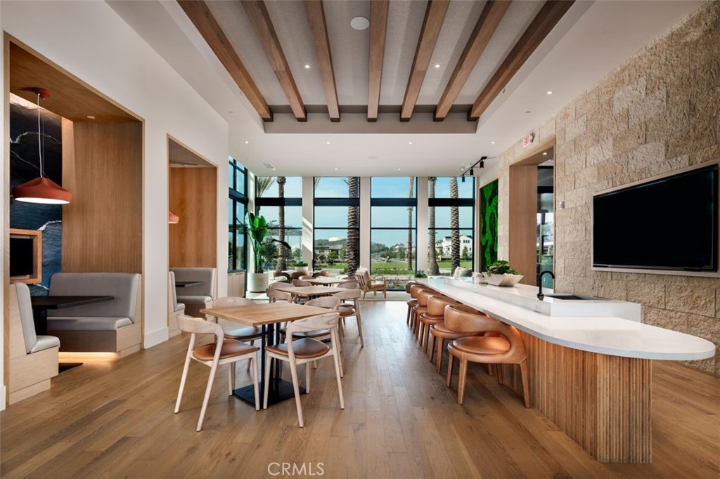 Furnished communal lounge with dining tables, a long bar, stone wall, and exposed ceiling beams.