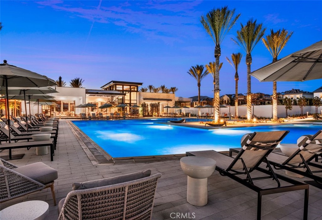 Outdoor pool at dusk with illuminated palm trees and rows of lounge chairs.