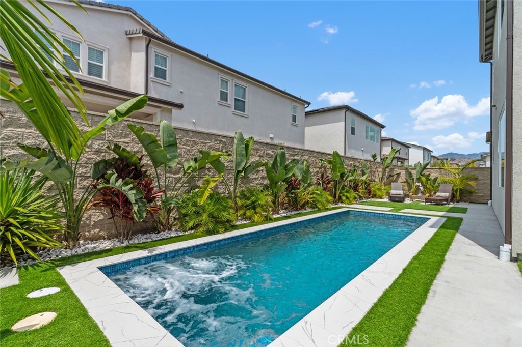 Backyard swimming pool bordered by tropical landscaping, white stone coping, and lounge chairs.