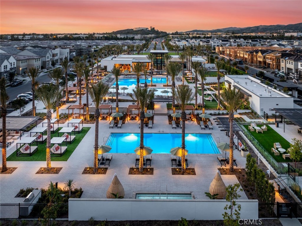Community pool area with illuminated pools, palm trees, and cabanas at dusk.