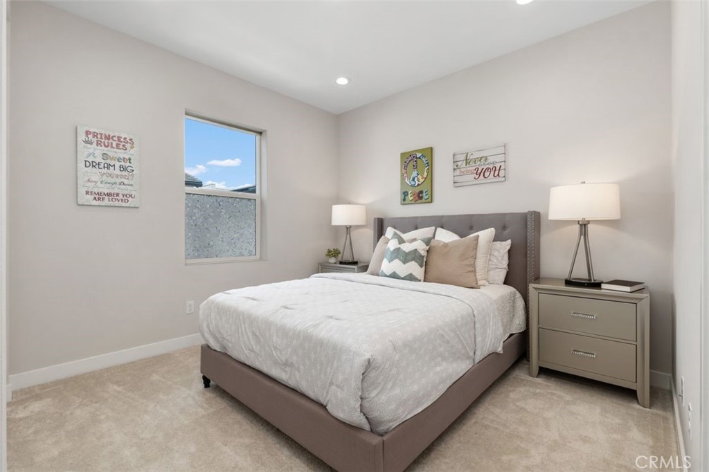 Staged bedroom with a large bed, gray upholstered headboard, white bedding, and matching bedside tables.