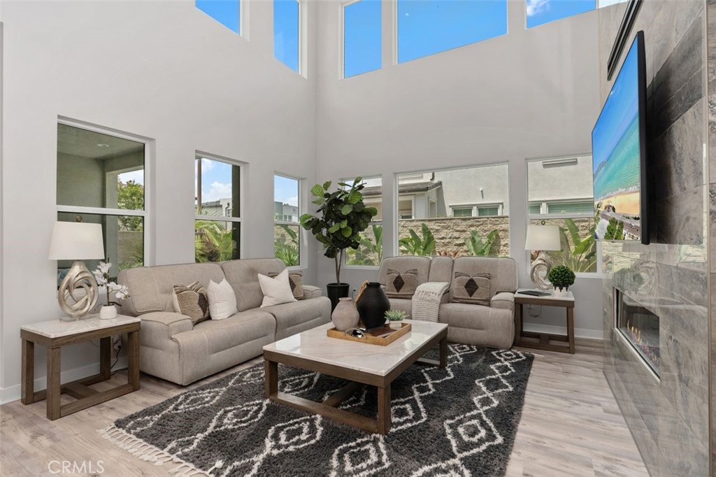 Staged living room with tall windows, beige sofas, and a stone fireplace wall.