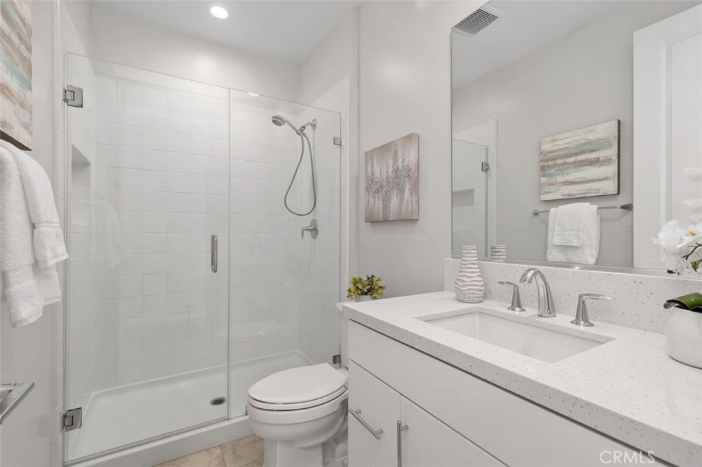 Bathroom with glass shower, white toilet, and speckled vanity beneath a large mirror.