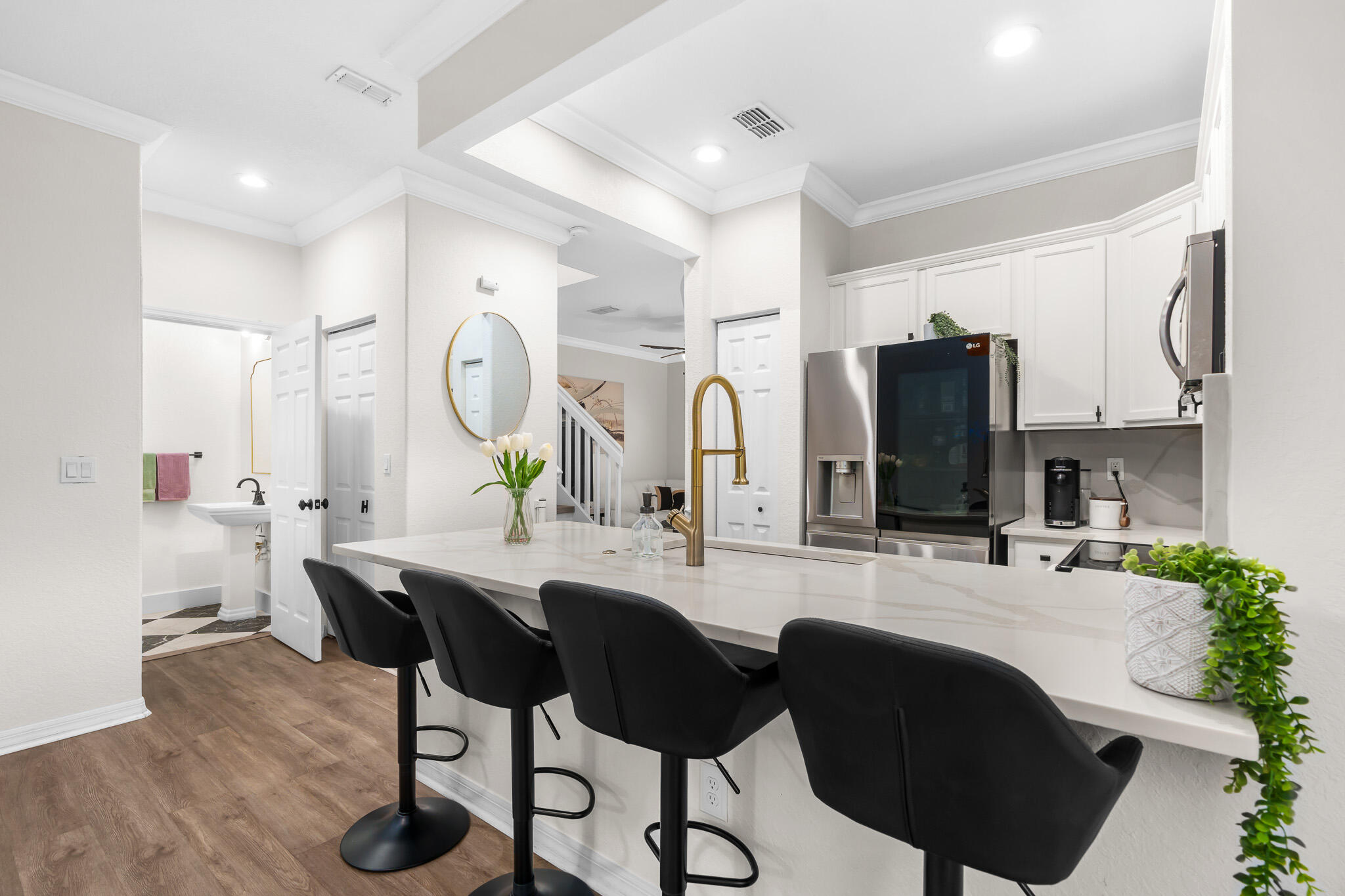 Kitchen with a large white island, gold faucet, black bar stools, and stainless steel appliances.