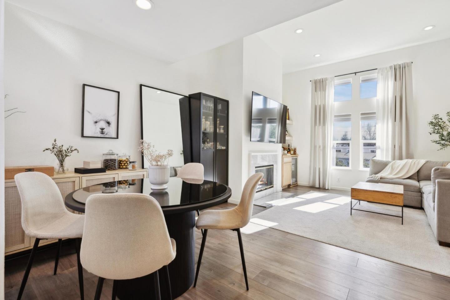 Open-plan living and dining room with a round black table, fireplace, tall windows, and gray sofa.