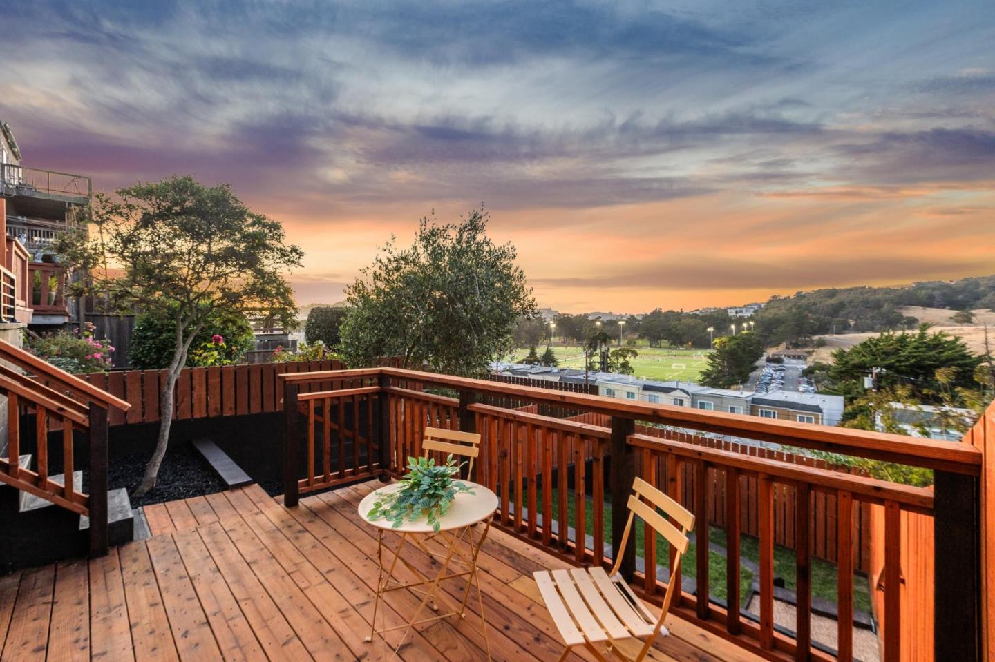 Wooden deck with outdoor seating overlooking playing fields and hills at sunset.