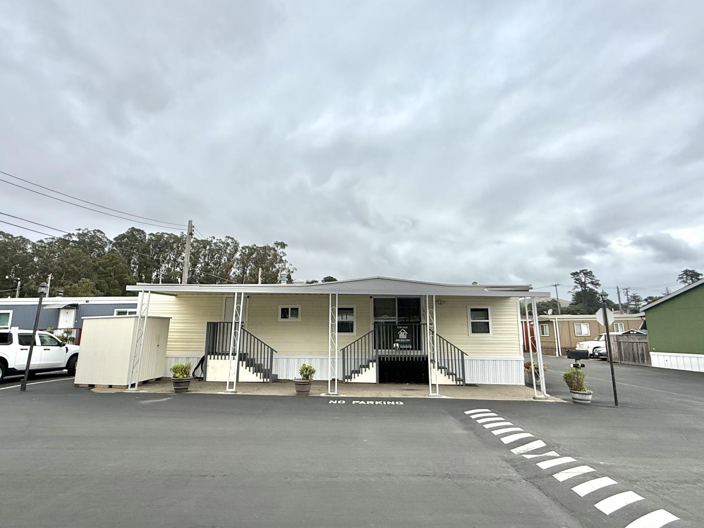Single-story manufactured home with a covered porch and black railings in a paved community parking area.