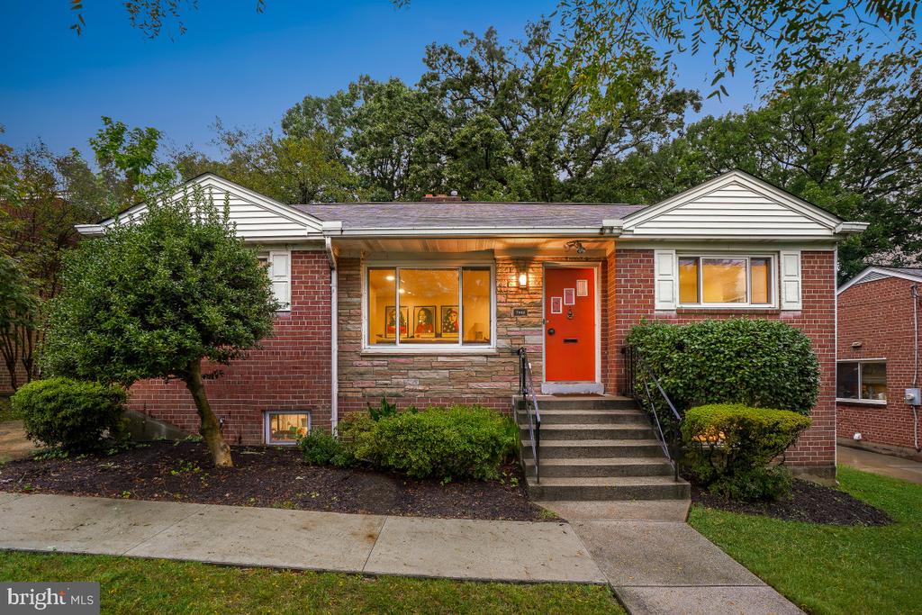 Brick house with white gables, a red front door, and landscaped shrubs.