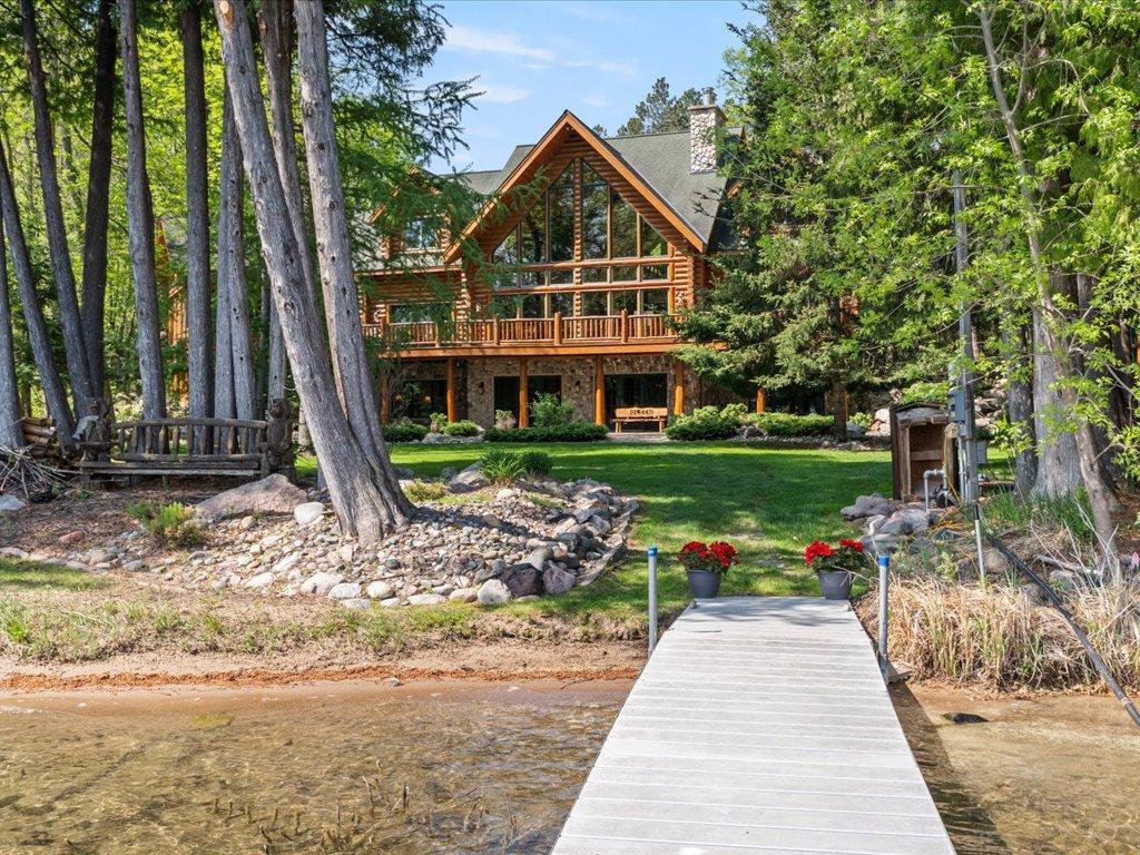 Wooded log home beside clear lake water, viewed from the end of a long dock.