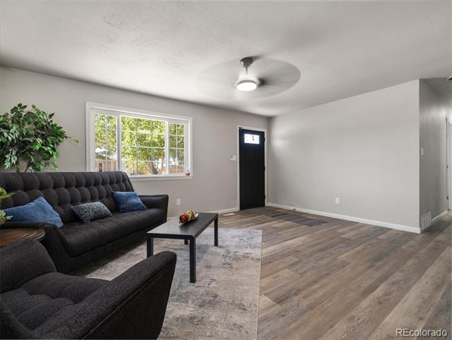 Living room with a dark sectional, large window, wood-look floors, and ceiling fan.