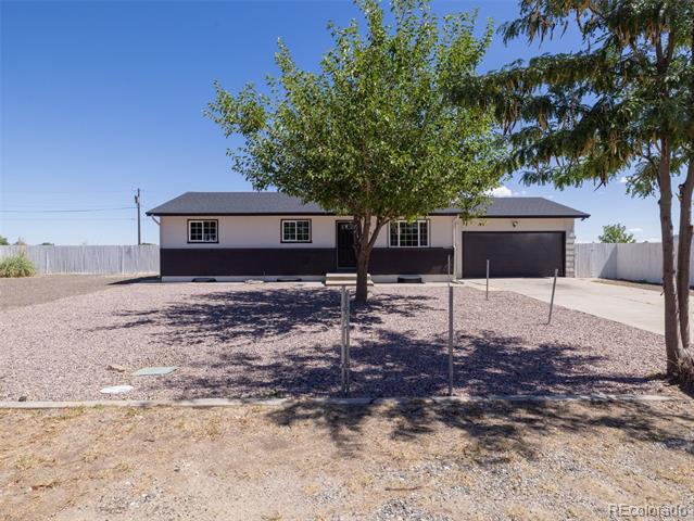 Single-story home with dark siding and a two-car garage behind a tree-shaded gravel yard.