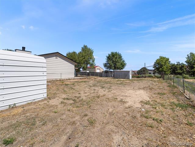 Fenced, dry yard with two outbuildings and scattered trees.